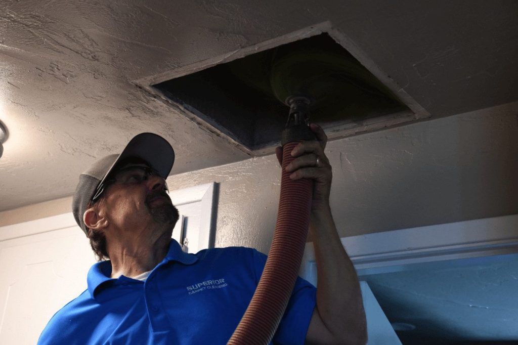 A technician reaching into an open ceiling vent to clean the duct behind it