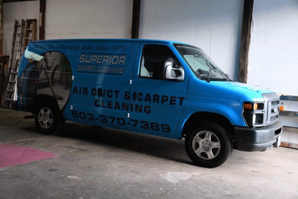 A branded air duct and carpet cleaning van parked inside the shop