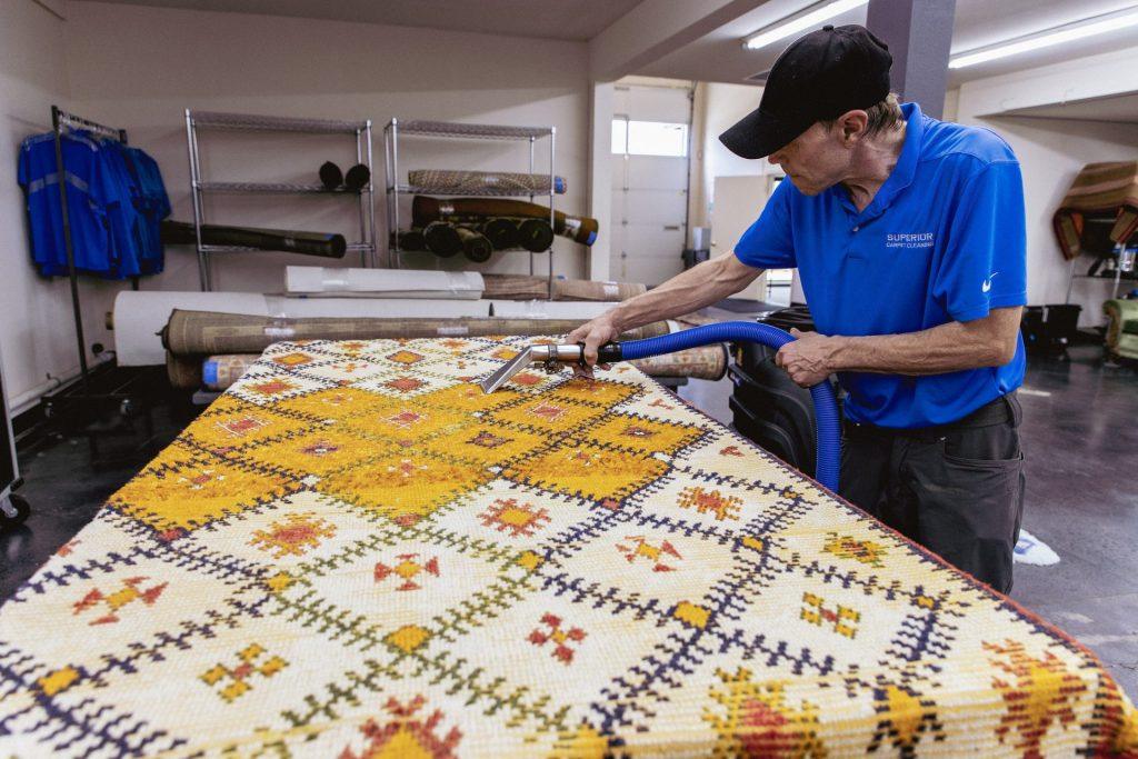 A technician cleaning a patterned rug spread on a table in the rug room